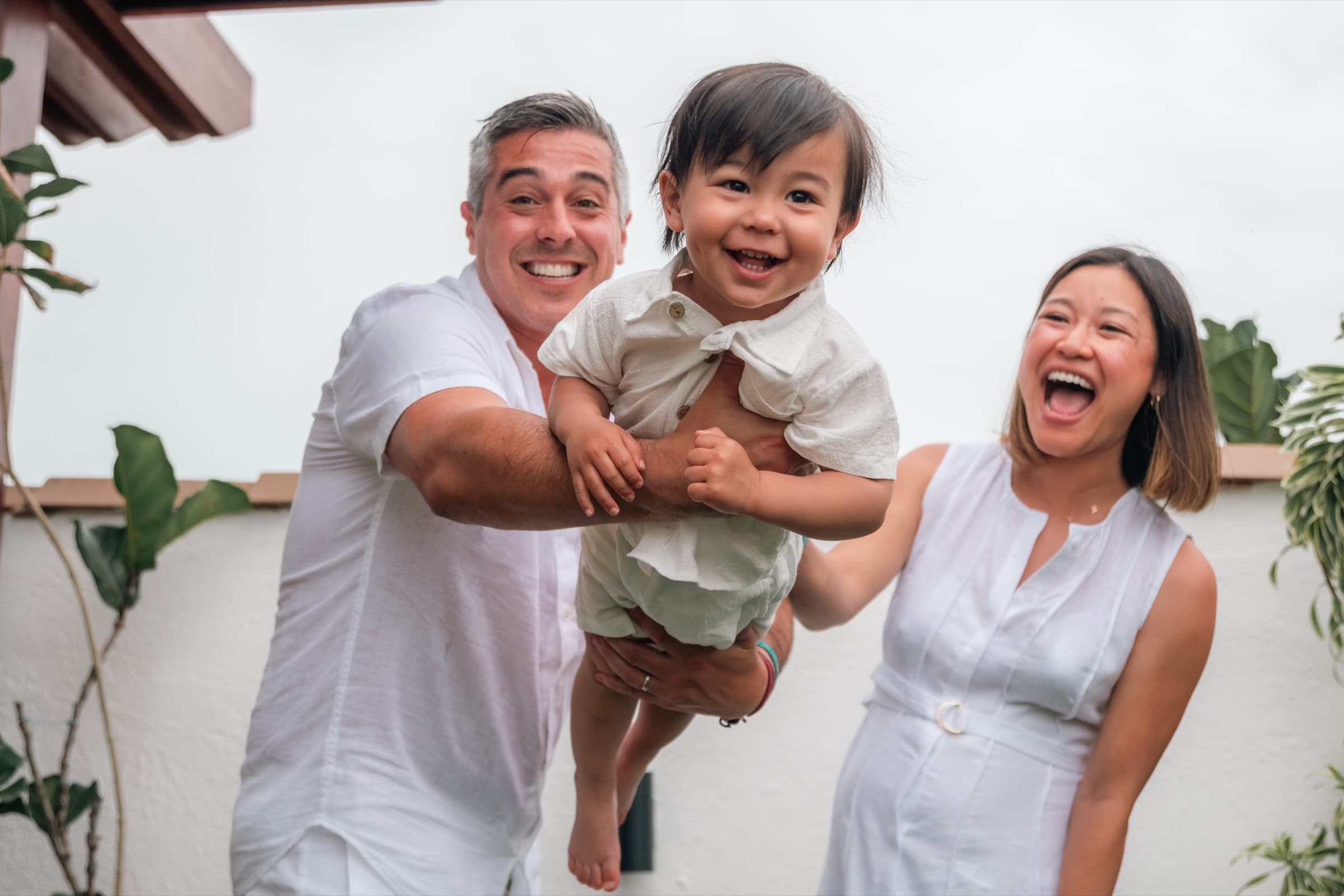 Parents holding their laughing toddler in a garden courtyard