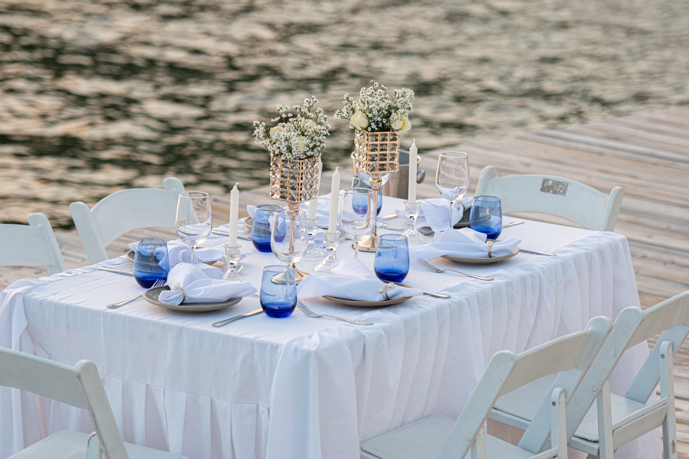 Reception table setting with blue glassware by the water