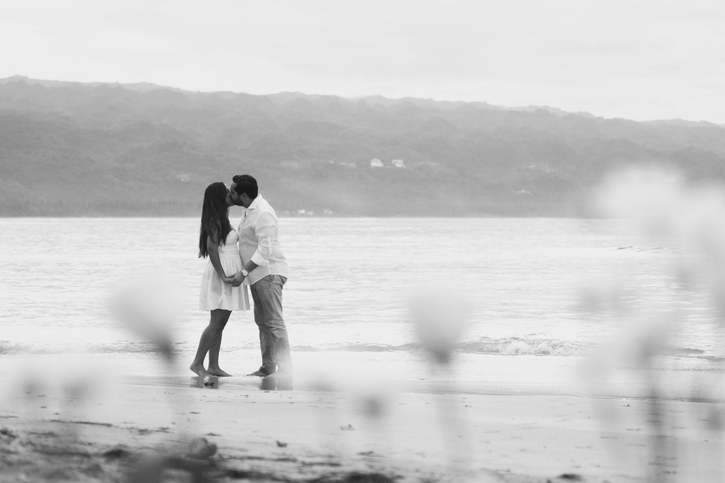 Angelica & Javier kissing on the beach, framed by blurred foreground florals
